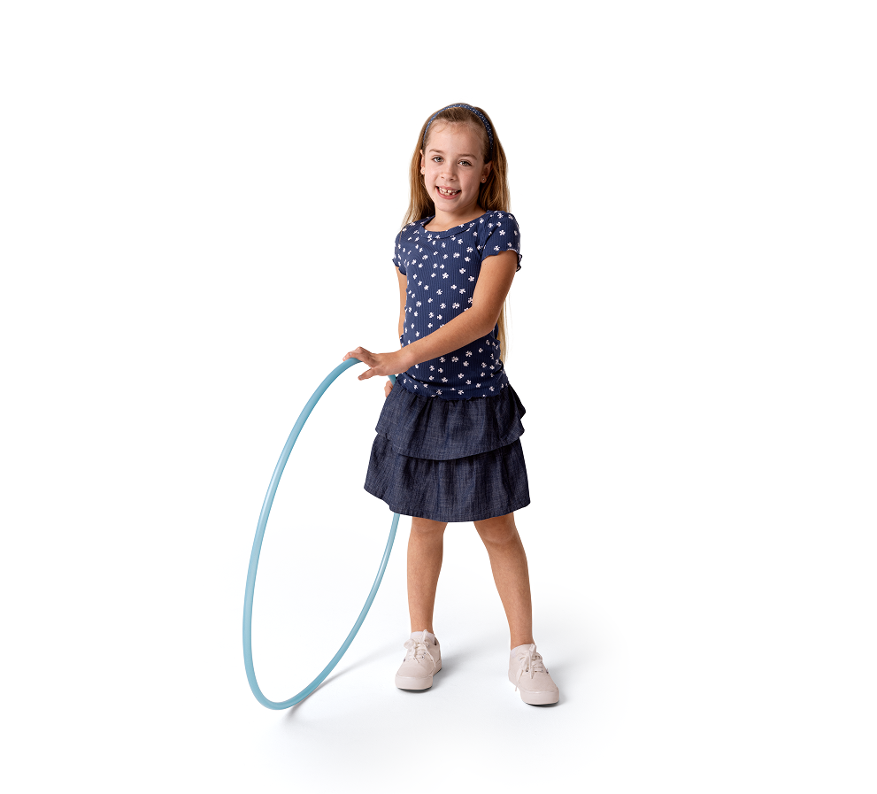 Cora, a person living with XLH, standing and smiling while holding a hula hoop