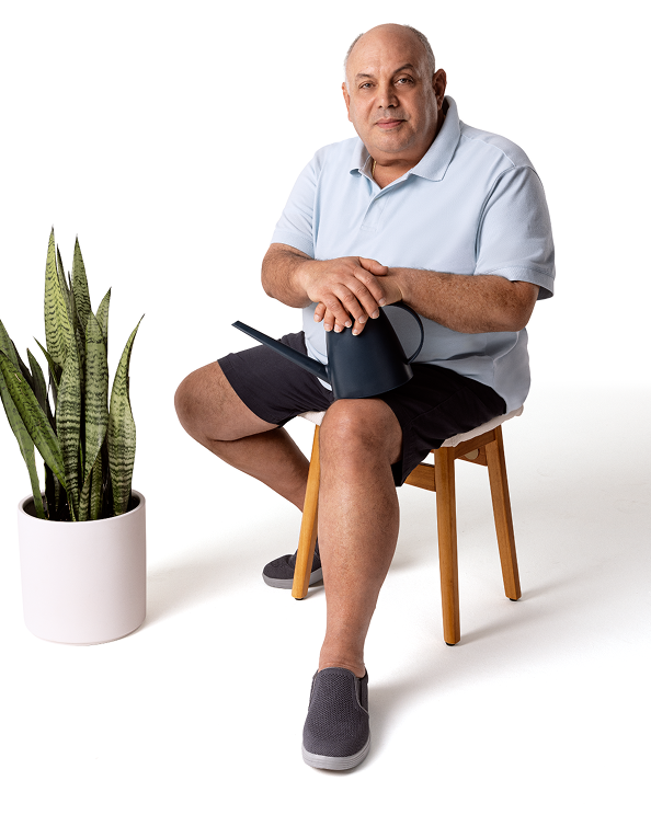Gilberto, a patient currently on CRYSVITA, smiling while sitting in a chair with a plant beside him